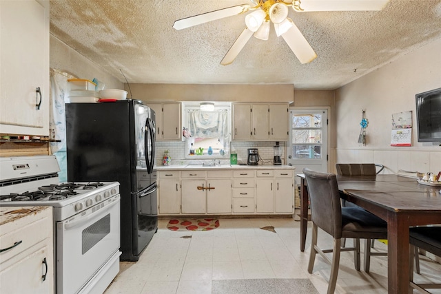 kitchen featuring a textured ceiling, cream cabinetry, white gas stove, and backsplash