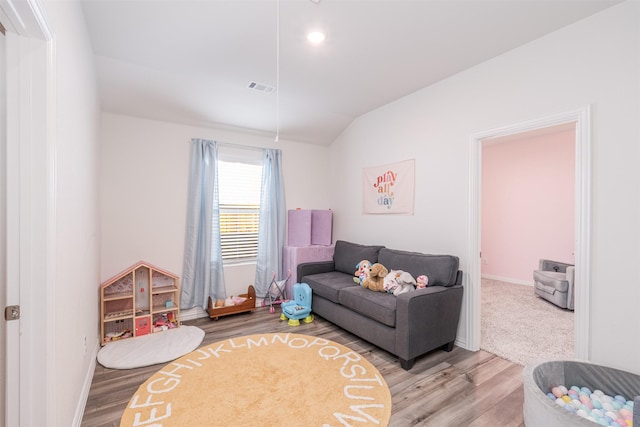 living room featuring lofted ceiling, wood finished floors, visible vents, and attic access