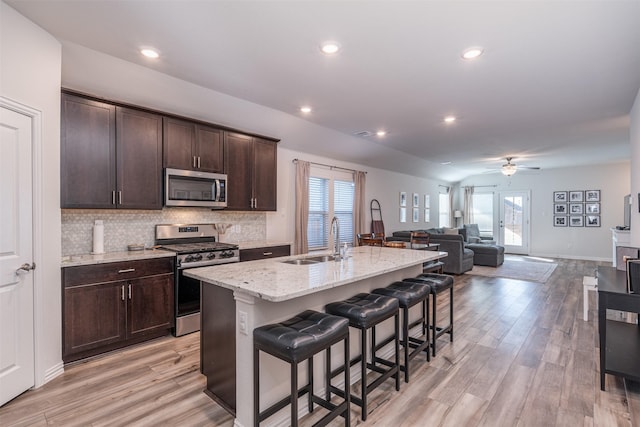 kitchen featuring stainless steel appliances, a sink, open floor plan, an island with sink, and a kitchen bar