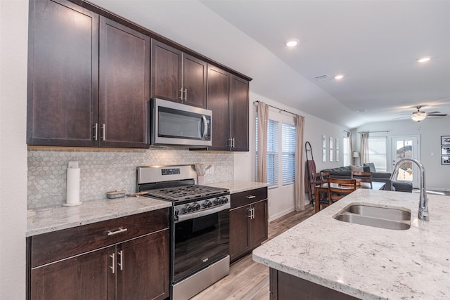 kitchen with light stone counters, lofted ceiling, appliances with stainless steel finishes, open floor plan, and a sink