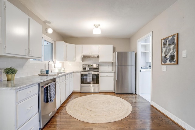 kitchen with appliances with stainless steel finishes, washer / dryer, decorative backsplash, sink, and white cabinetry