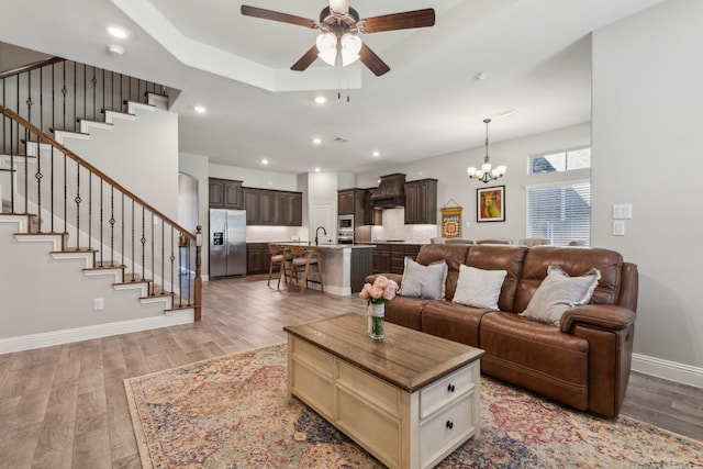 living room with a tray ceiling, light hardwood / wood-style flooring, sink, and ceiling fan with notable chandelier