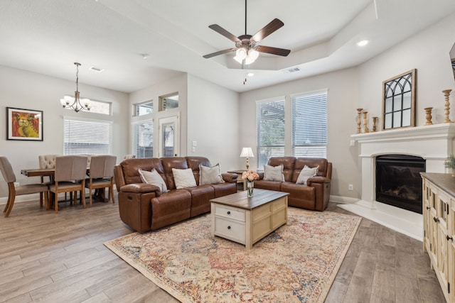 living room with a tray ceiling, light hardwood / wood-style floors, and ceiling fan with notable chandelier