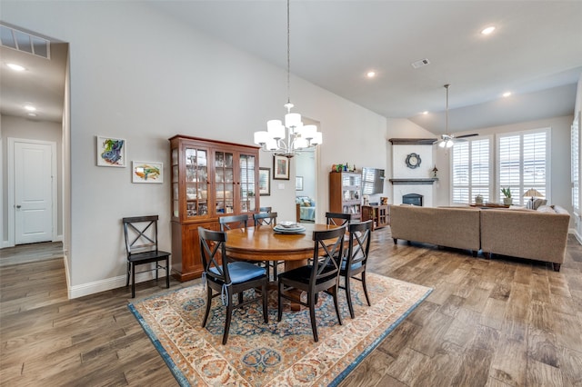 dining room with ceiling fan with notable chandelier, high vaulted ceiling, and wood-type flooring