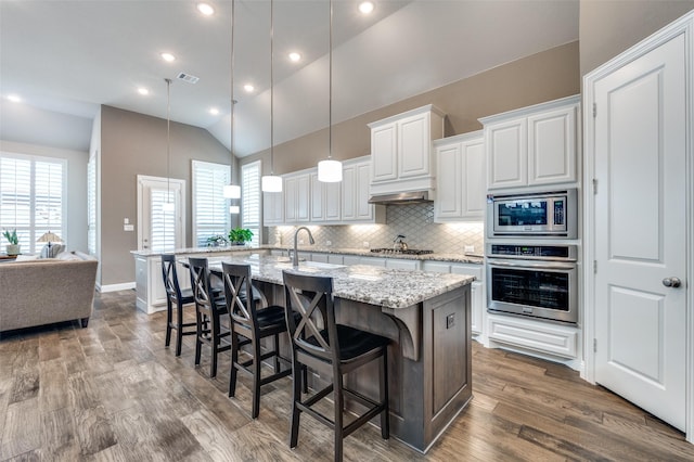 kitchen featuring appliances with stainless steel finishes, a kitchen breakfast bar, light stone counters, white cabinetry, and a kitchen island with sink