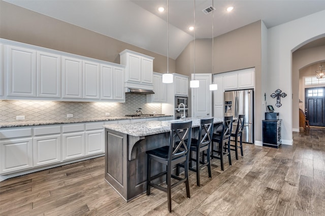 kitchen featuring appliances with stainless steel finishes, a kitchen bar, hanging light fixtures, white cabinets, and an island with sink