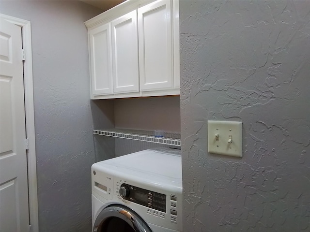 laundry room featuring washer / dryer, cabinet space, and a textured wall