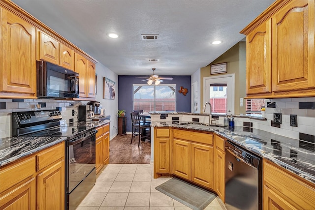 kitchen featuring light tile patterned floors, sink, dark stone counters, black appliances, and kitchen peninsula