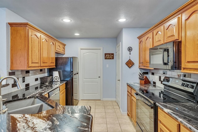 kitchen featuring tasteful backsplash, dark stone counters, black appliances, light tile patterned floors, and sink