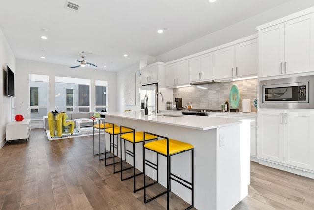 kitchen with appliances with stainless steel finishes, sink, white cabinets, an island with sink, and a breakfast bar area