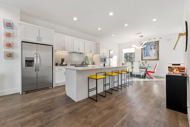 kitchen with an island with sink, decorative light fixtures, appliances with stainless steel finishes, white cabinets, and a kitchen breakfast bar