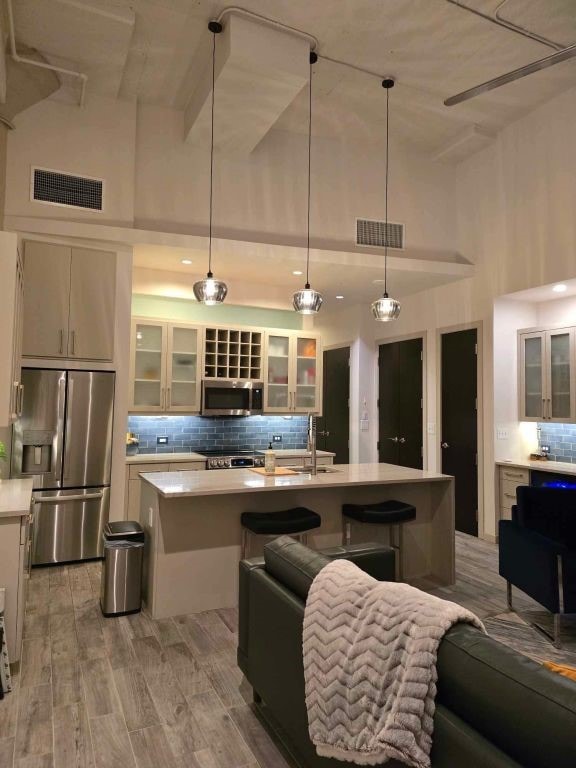 kitchen with light hardwood / wood-style flooring, decorative light fixtures, stainless steel appliances, a kitchen island with sink, and decorative backsplash