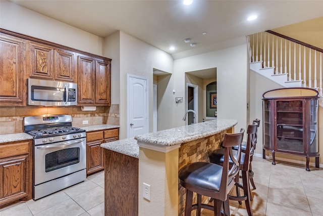 5320 Locust Dr, Mckinney, TX 75070 - kitchen with appliances with stainless steel finishes, backsplash, light tile patterned floors, light stone counters, and a kitchen bar