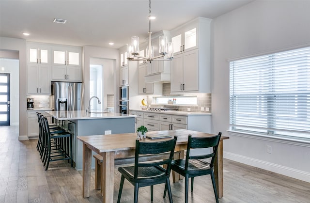 kitchen featuring appliances with stainless steel finishes, white cabinetry, pendant lighting, and an island with sink