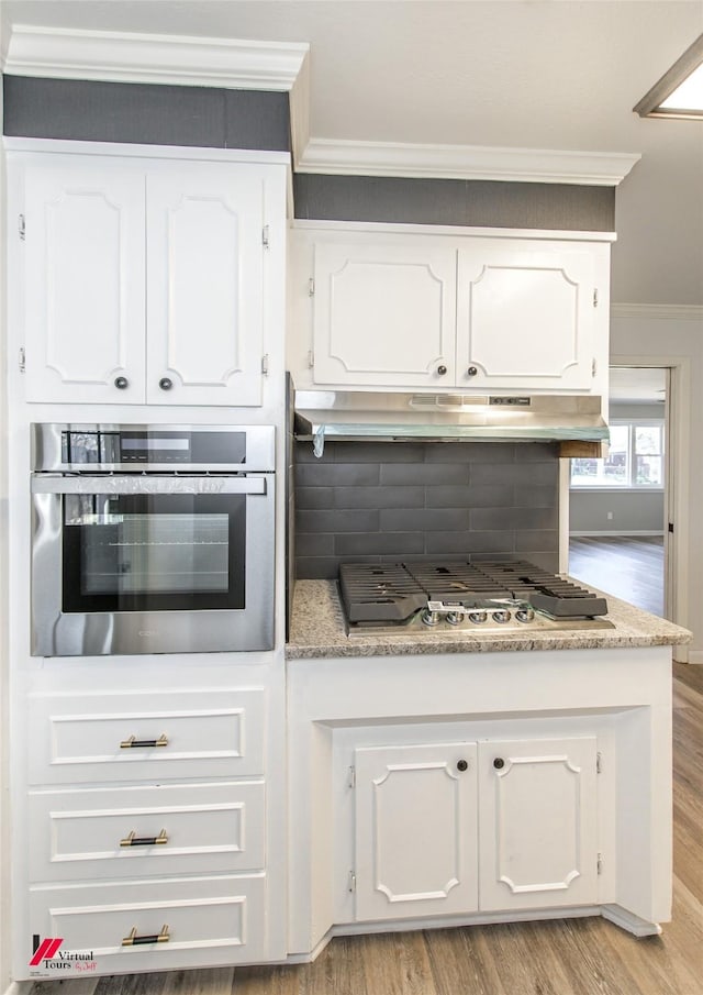 kitchen with appliances with stainless steel finishes, ornamental molding, light wood-type flooring, and white cabinets