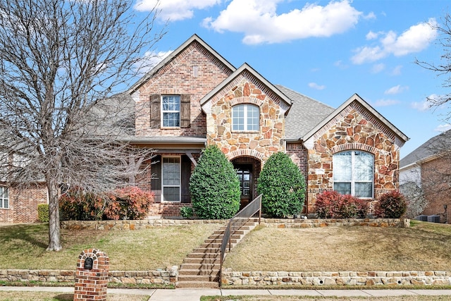 view of front of property featuring stone siding, brick siding, roof with shingles, and a front yard