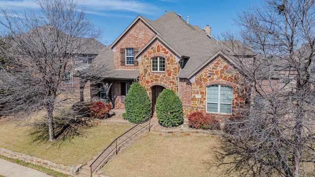 view of front of home featuring stone siding, a front lawn, a shingled roof, and brick siding