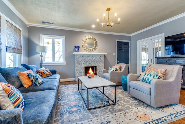 living area with visible vents, a tiled fireplace, ornamental molding, wood finished floors, and french doors