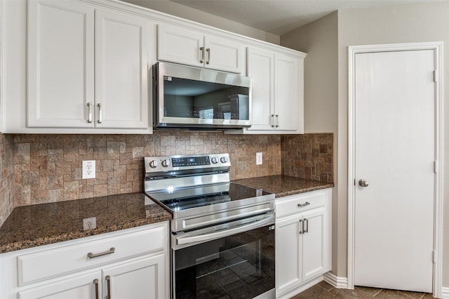 kitchen featuring appliances with stainless steel finishes, white cabinetry, dark stone countertops, and backsplash