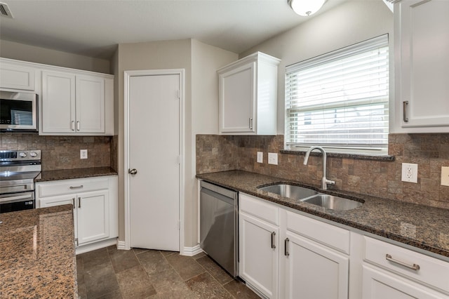 kitchen with white cabinetry, stainless steel appliances, sink, backsplash, and dark stone counters