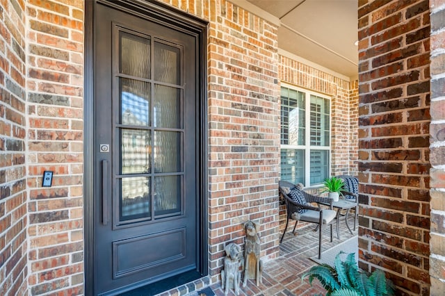 view of exterior entry featuring brick siding and covered porch