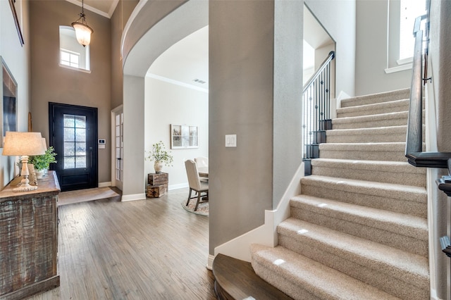 foyer entrance with a towering ceiling, wood finished floors, crown molding, baseboards, and arched walkways