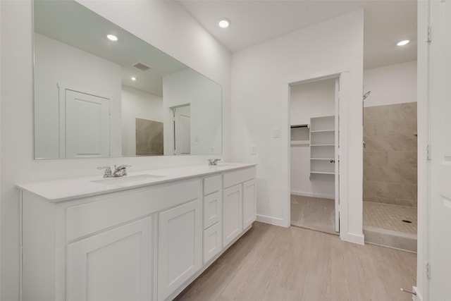 full bathroom with a sink, tiled shower, and wood finished floors