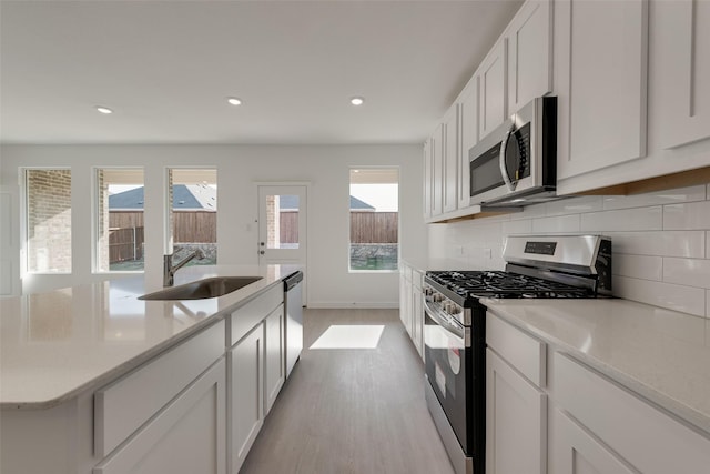 kitchen featuring tasteful backsplash, light wood-type flooring, white cabinetry, appliances with stainless steel finishes, and a sink
