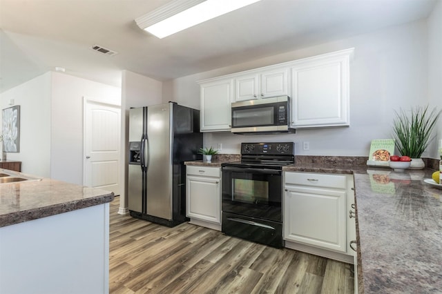 kitchen featuring stainless steel appliances, dark countertops, visible vents, white cabinets, and wood finished floors