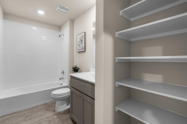 bathroom featuring toilet, wood finished floors, visible vents, vanity, and shower / washtub combination