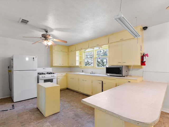 kitchen featuring white appliances, a textured ceiling, ceiling fan, a kitchen island, and kitchen peninsula