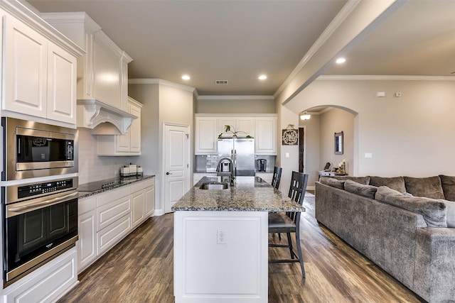 kitchen with stainless steel appliances, white cabinetry, an island with sink, and dark stone counters