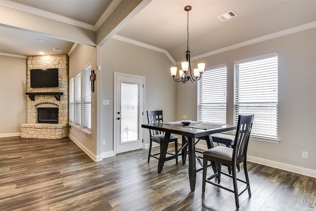 dining area with ornamental molding, a stone fireplace, an inviting chandelier, and dark wood-type flooring