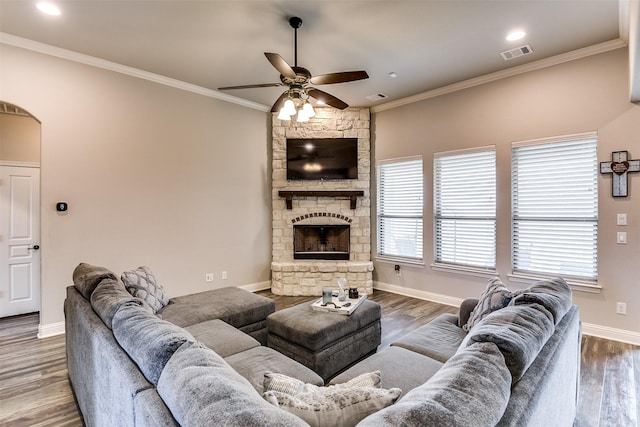 living room with ceiling fan, wood-type flooring, a stone fireplace, and ornamental molding