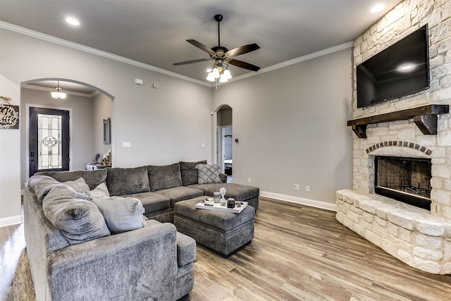 living room featuring ceiling fan, a stone fireplace, crown molding, and hardwood / wood-style floors