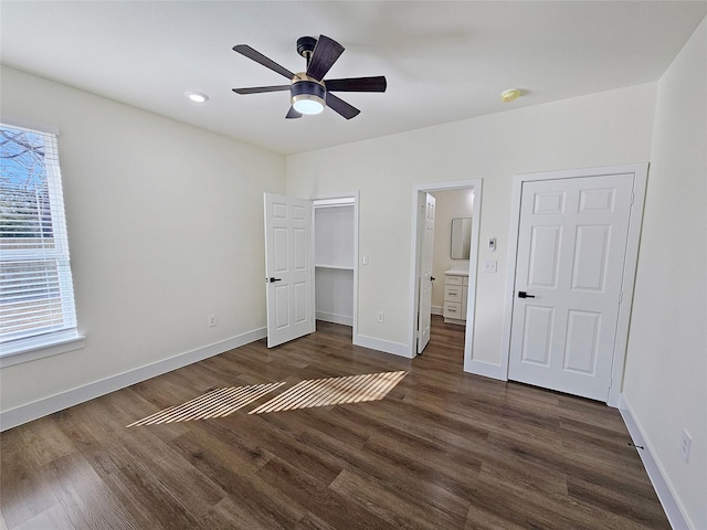 unfurnished bedroom with connected bathroom, a walk in closet, a closet, ceiling fan, and dark hardwood / wood-style floors