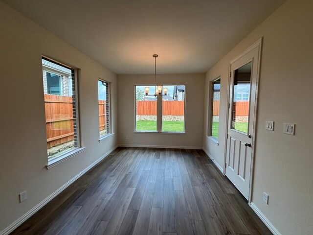 unfurnished dining area featuring dark wood-type flooring, a chandelier, and baseboards
