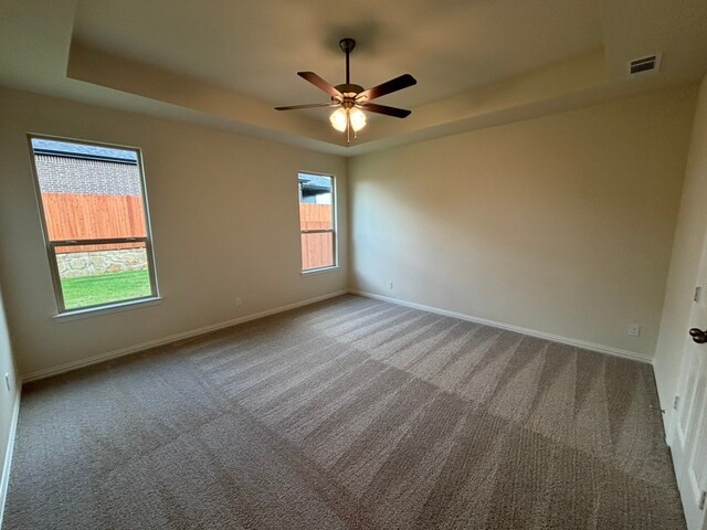 carpeted spare room with visible vents, a tray ceiling, and baseboards