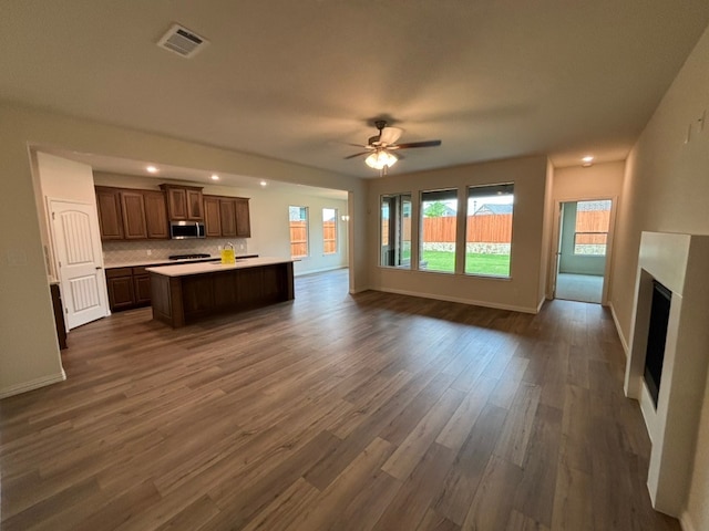 unfurnished living room with a ceiling fan, visible vents, baseboards, and dark wood finished floors