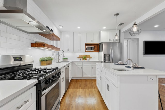 kitchen with stainless steel appliances, light countertops, white cabinetry, a sink, and wall chimney range hood