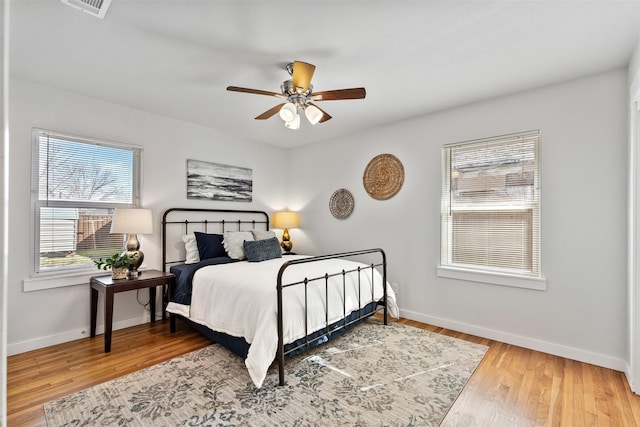 bedroom with ceiling fan, visible vents, baseboards, and wood finished floors