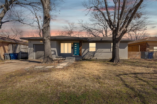 mid-century home with an attached garage, fence, driveway, a lawn, and stucco siding