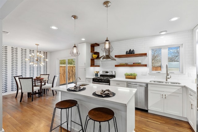 kitchen featuring stainless steel appliances, a kitchen island with sink, light countertops, and a sink