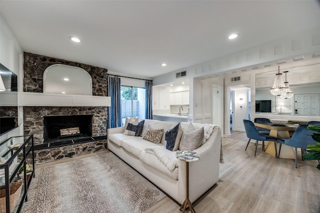 living room featuring light wood-type flooring, sink, and a stone fireplace