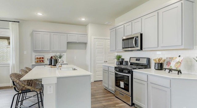 kitchen featuring a breakfast bar area, stainless steel appliances, light hardwood / wood-style floors, sink, and a kitchen island with sink