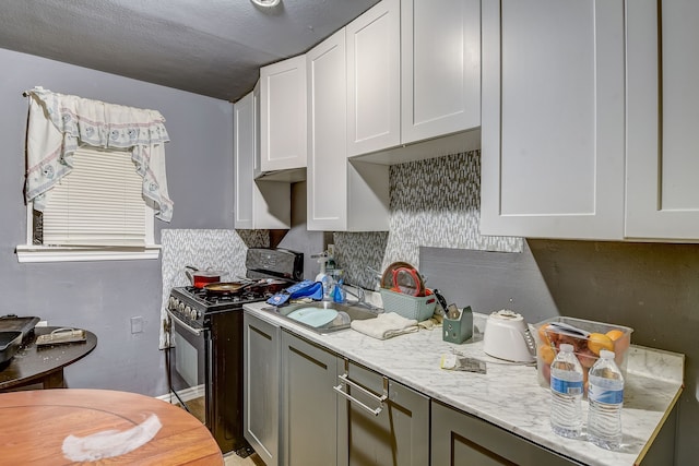 kitchen featuring gas stove, backsplash, sink, white cabinetry, and light stone countertops