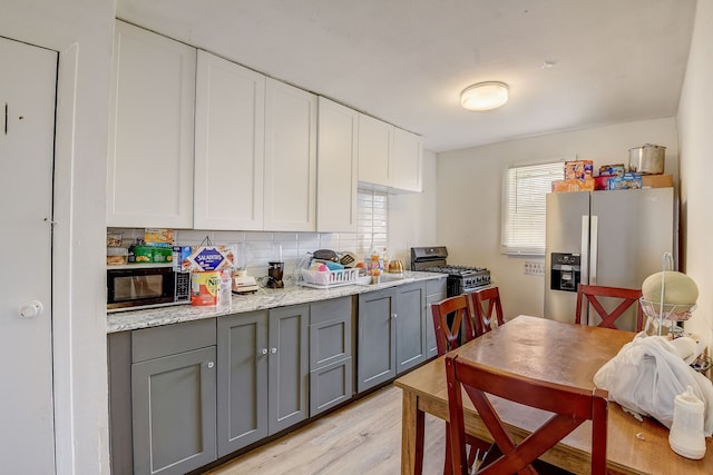 kitchen with stainless steel appliances, white cabinets, light hardwood / wood-style floors, backsplash, and gray cabinets