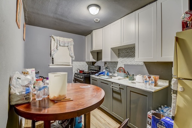 kitchen featuring refrigerator, gray cabinetry, white cabinets, and stainless steel range with gas stovetop