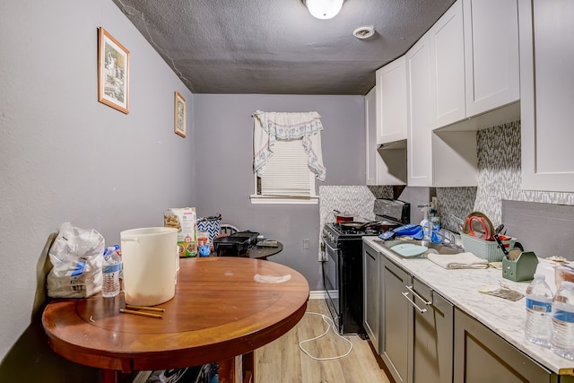 kitchen featuring light stone countertops, a textured ceiling, decorative backsplash, light hardwood / wood-style floors, and black gas range oven