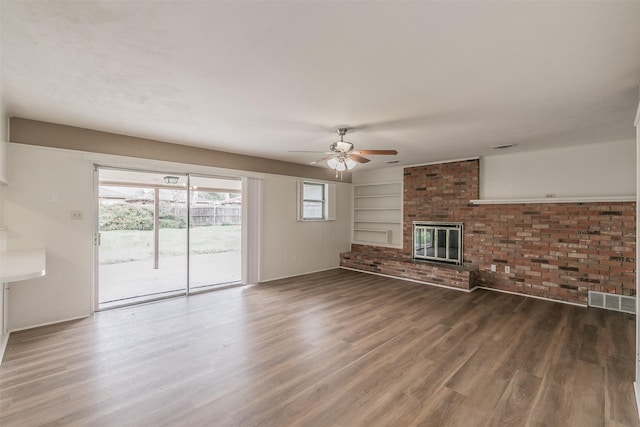 unfurnished living room with ceiling fan, wood-type flooring, a brick fireplace, and built in features